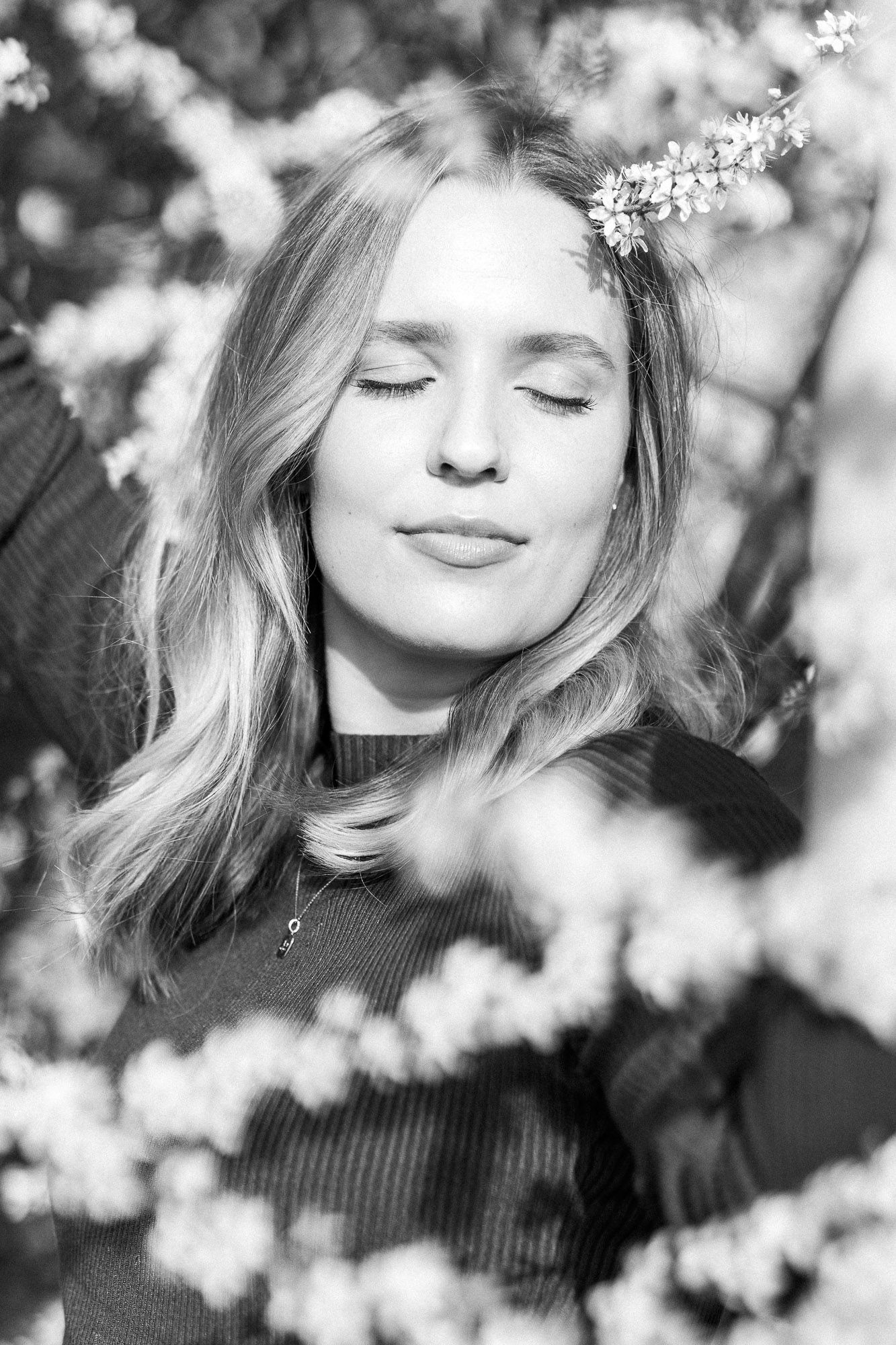 Serene portrait in black and white among blooming spring branches with delicate white flowers creating a dreamy atmosphere.