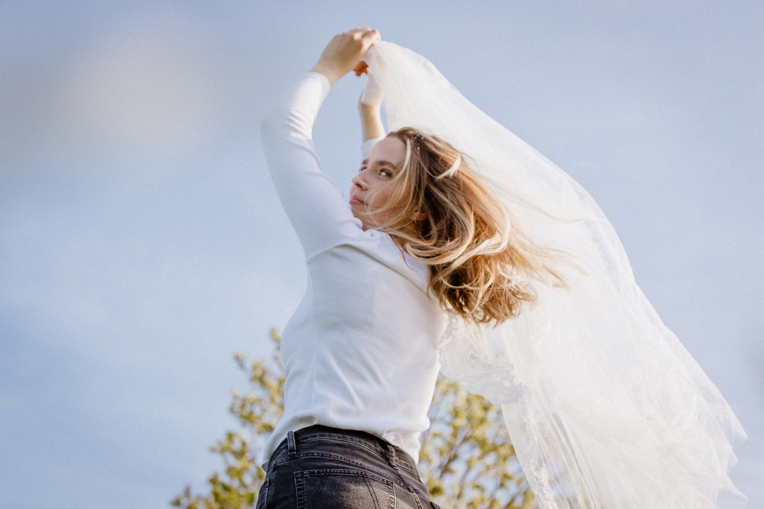 Dynamic portrait with flowing white fabric against blue sky capturing movement and freedom.