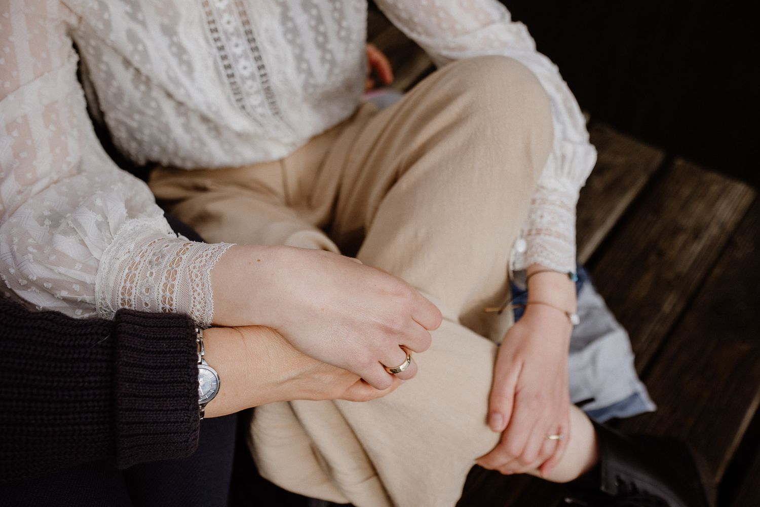 Close-up of hands resting on beige pants while sitting on wooden surface.