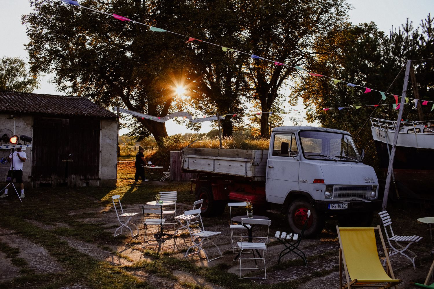 A vintage white truck parked at sunset with outdoor seating and string lights in a rural setting.
