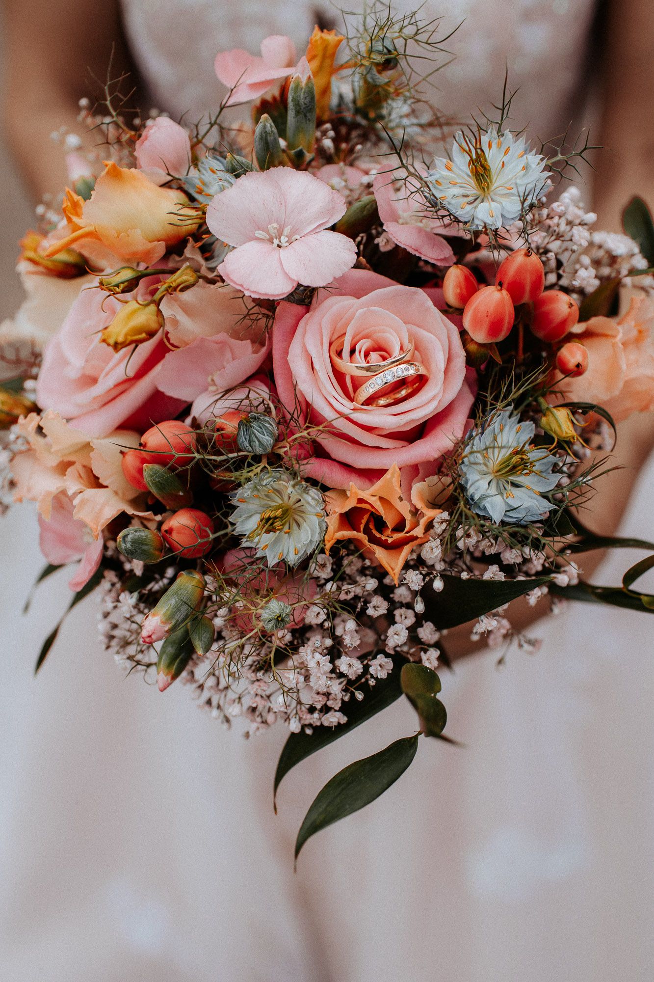 Romantic wedding bouquet with pink roses, orange blooms and delicate baby's breath.