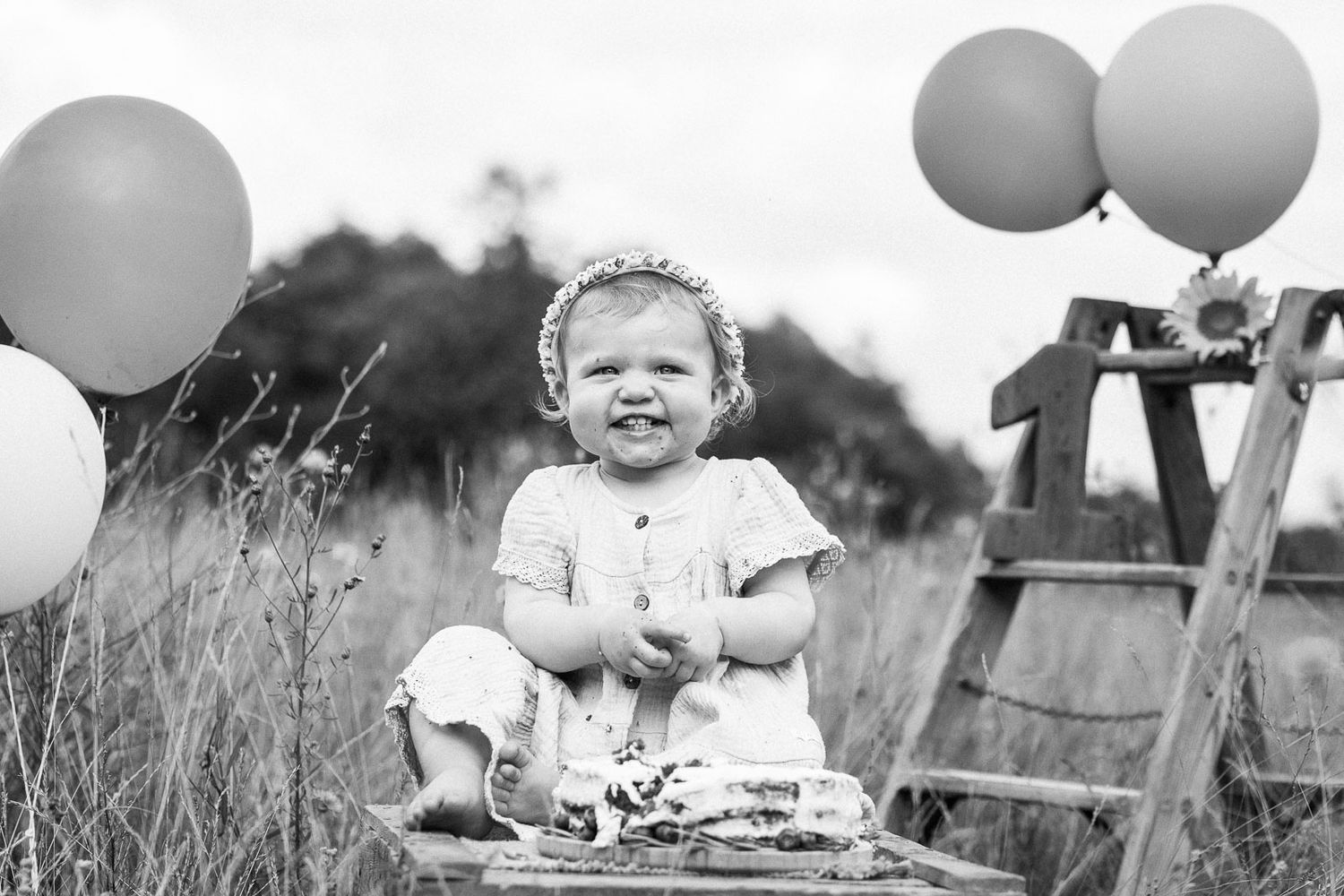 Black and white capture of happy celebration with balloons and wooden ladder outdoors.