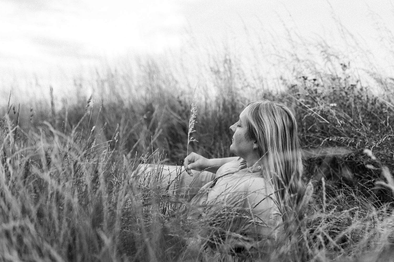Artistic black and white portrait of person lying in field of tall grass.