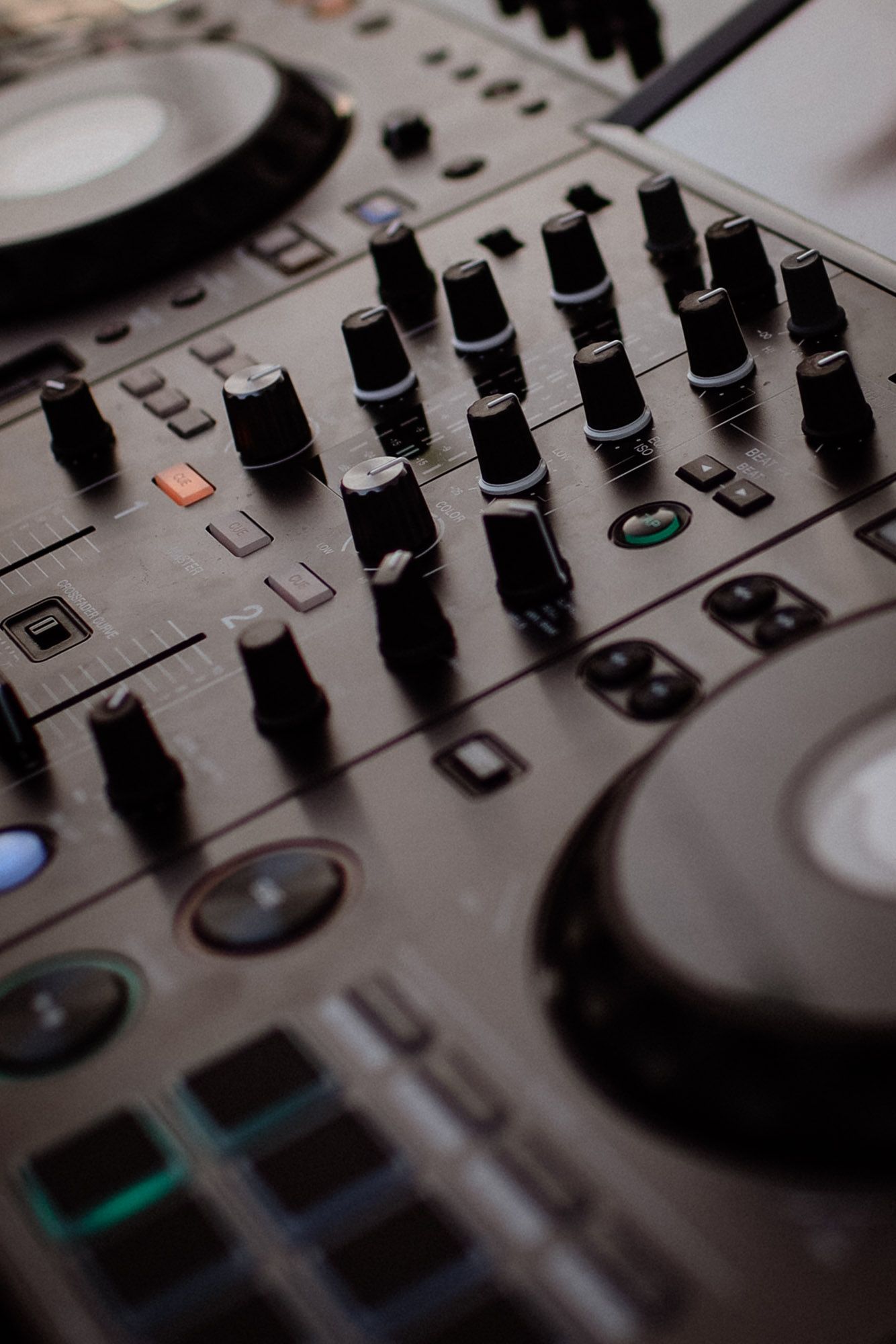Professional DJ mixer control panel with multiple knobs and faders in dramatic lighting.