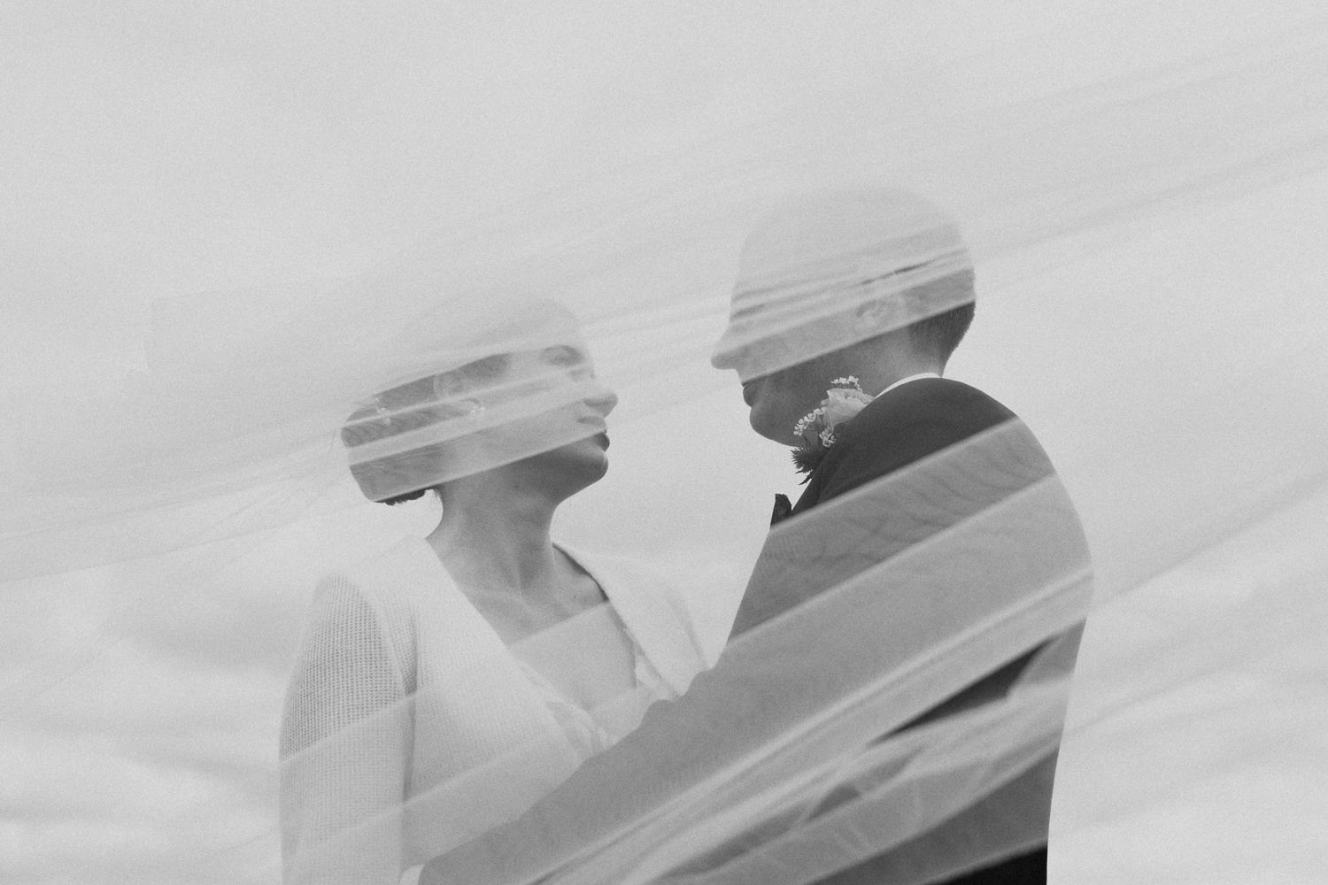 Double exposure black and white photo of two figures with static distortion effect against cloudy sky.