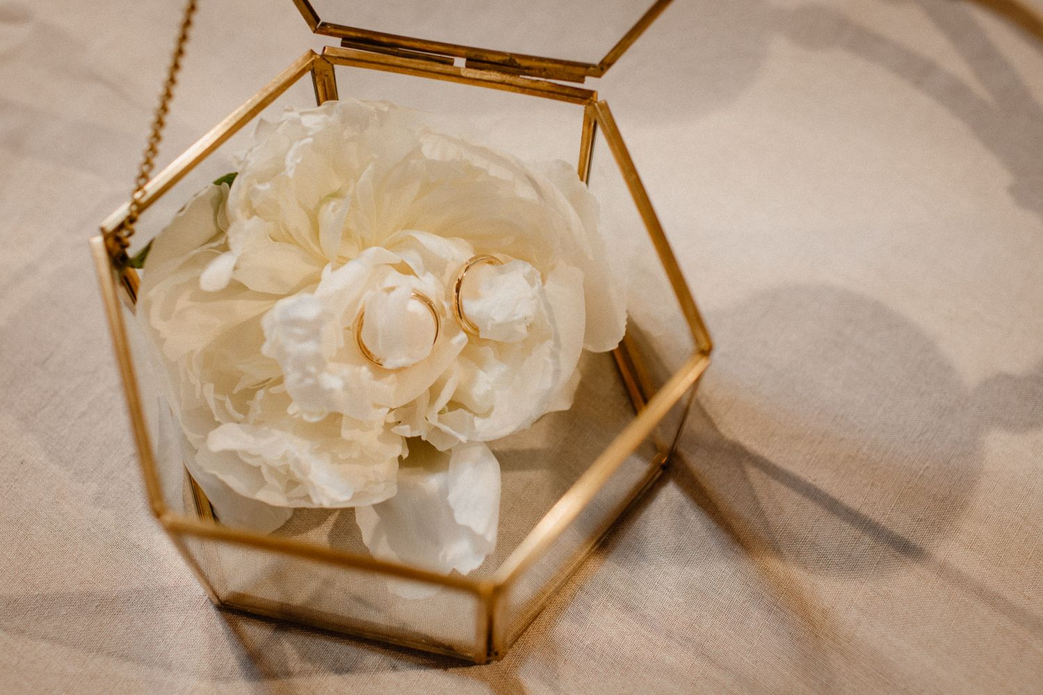 Gold geometric glass display boxes with white floral decorations on light surface.