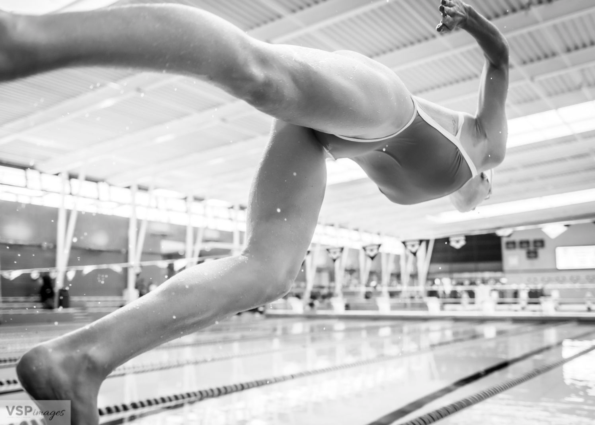 Black and white photo of a swimmer diving into a pool at the start of a race.