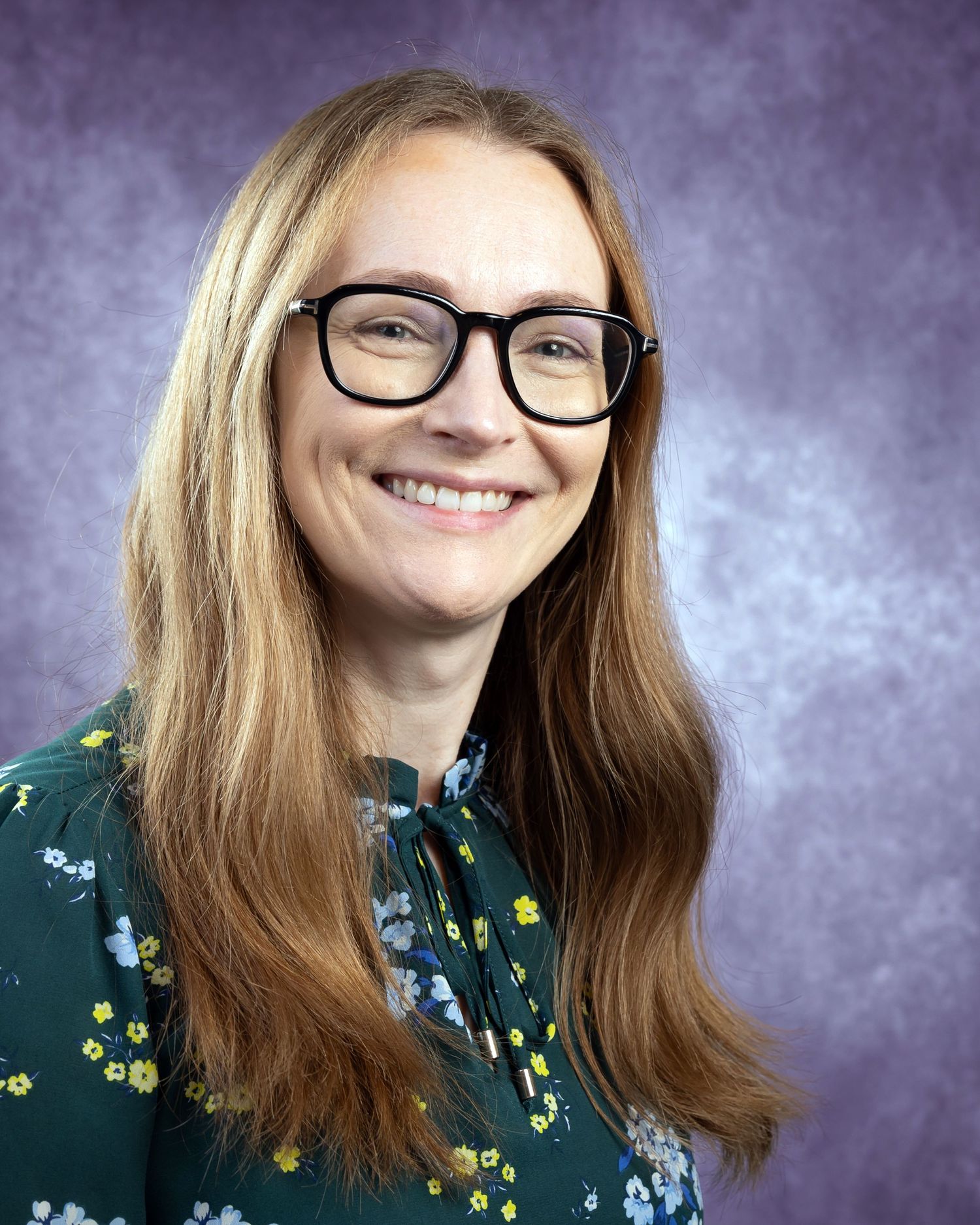 A person with long blonde hair wearing glasses and a floral print green top smiles in a series of professional headshots.