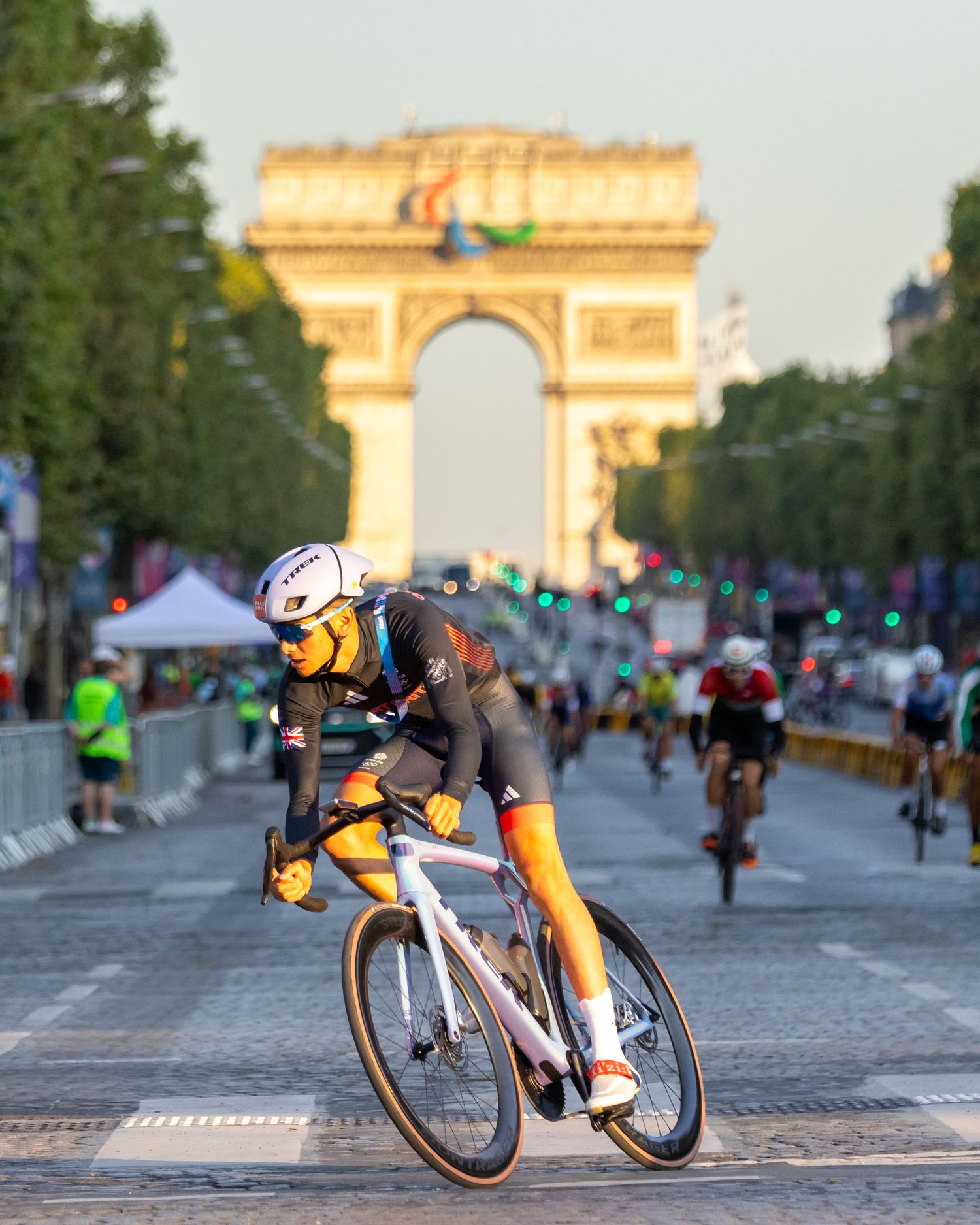 A british triathlete in racing gear speeds past the iconic Arc de Triomphe in Paris during a cycling event.