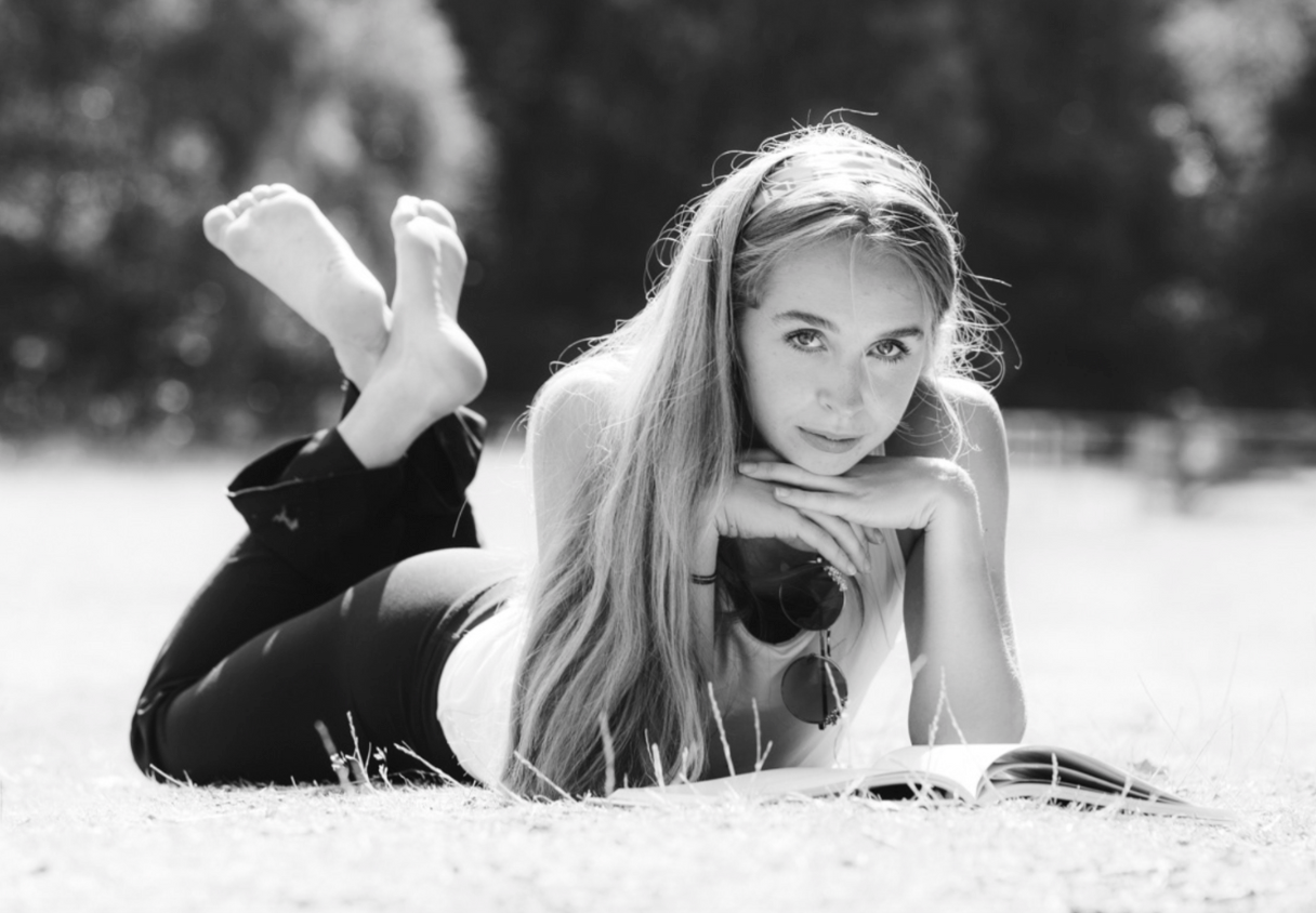 Black and white portrait of person lying on grass reading outdoors.