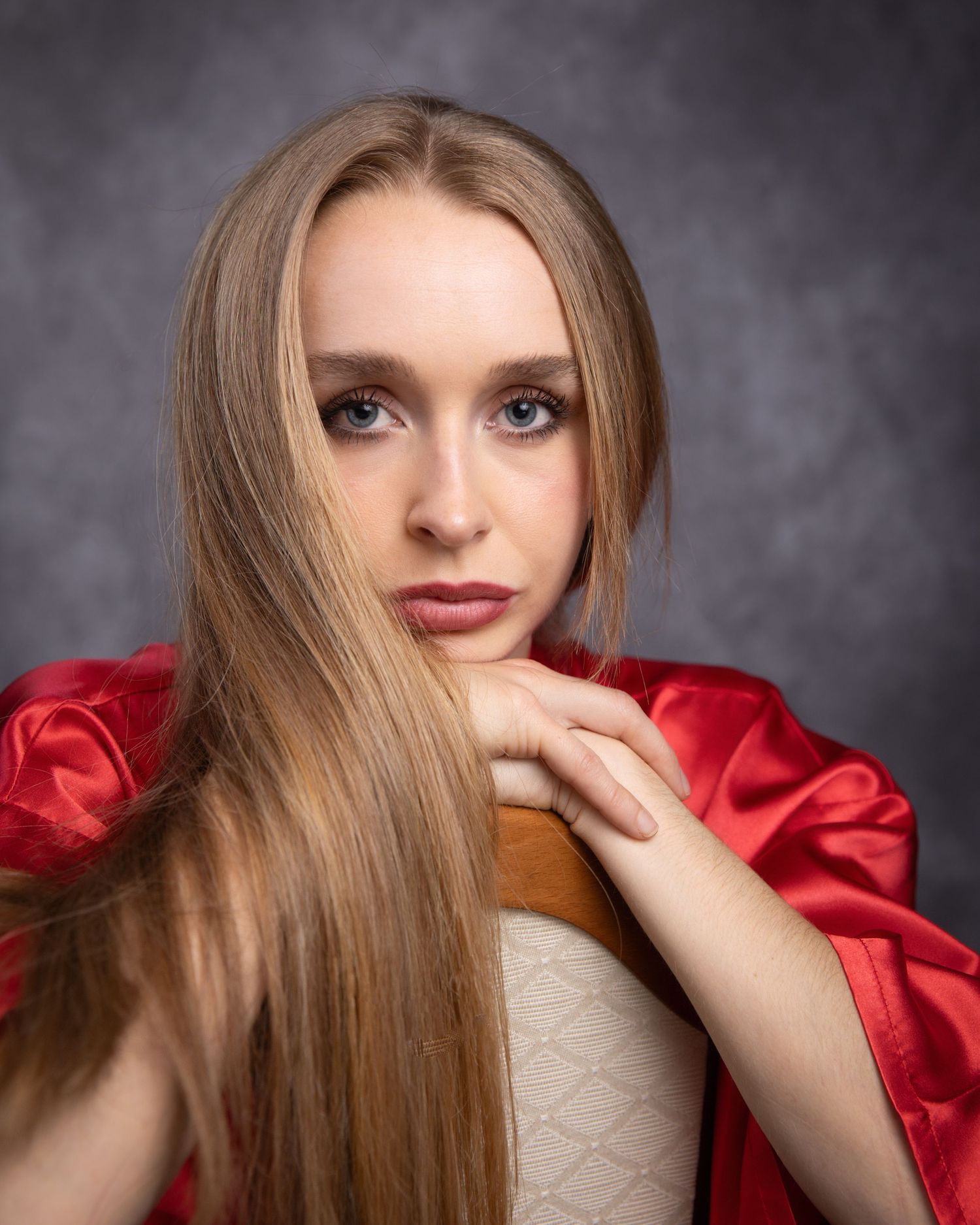 A fashion portrait series with long blonde hair and a red satin top against a dark gray studio background.