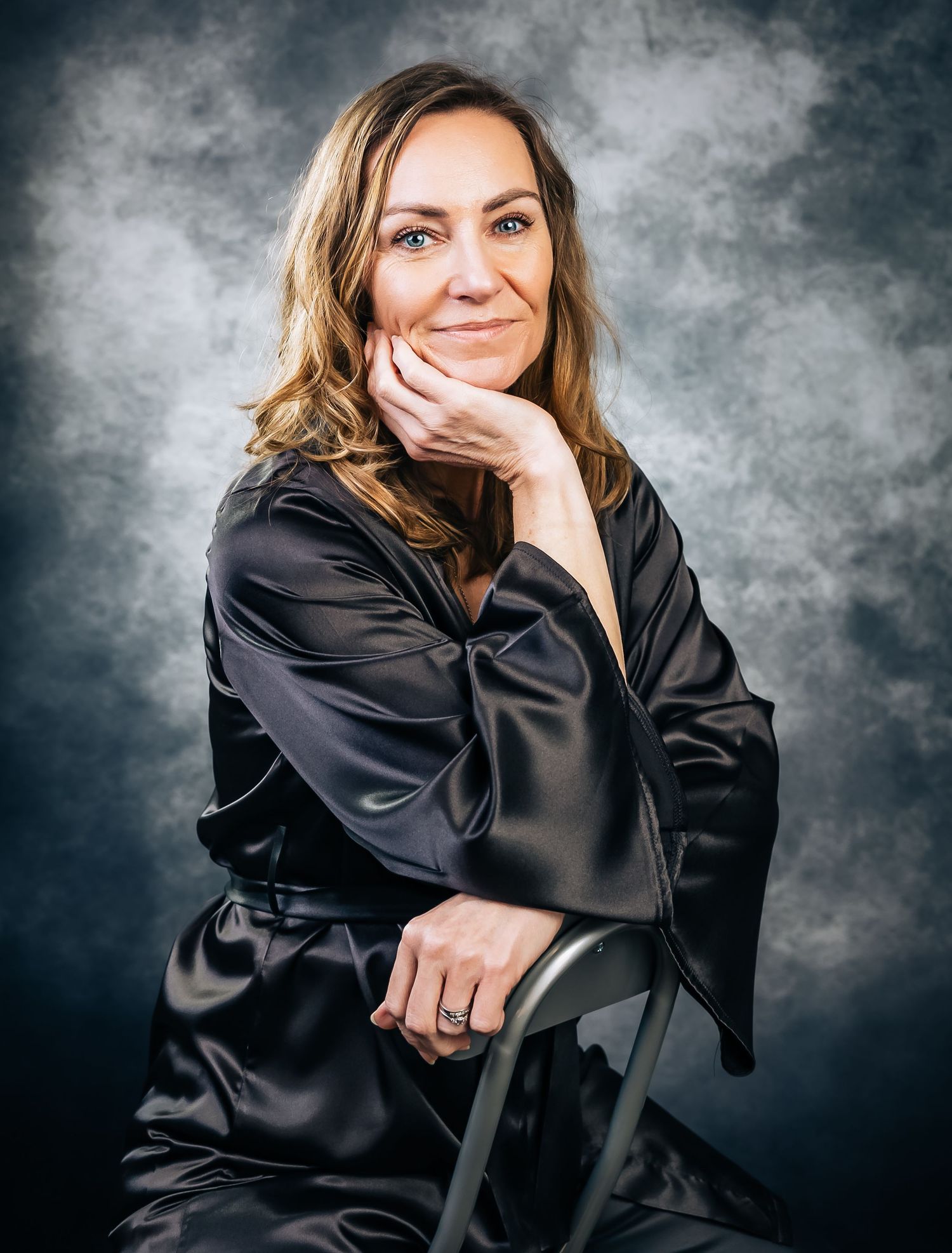 Professional portrait in black silk robe against moody gray studio background.