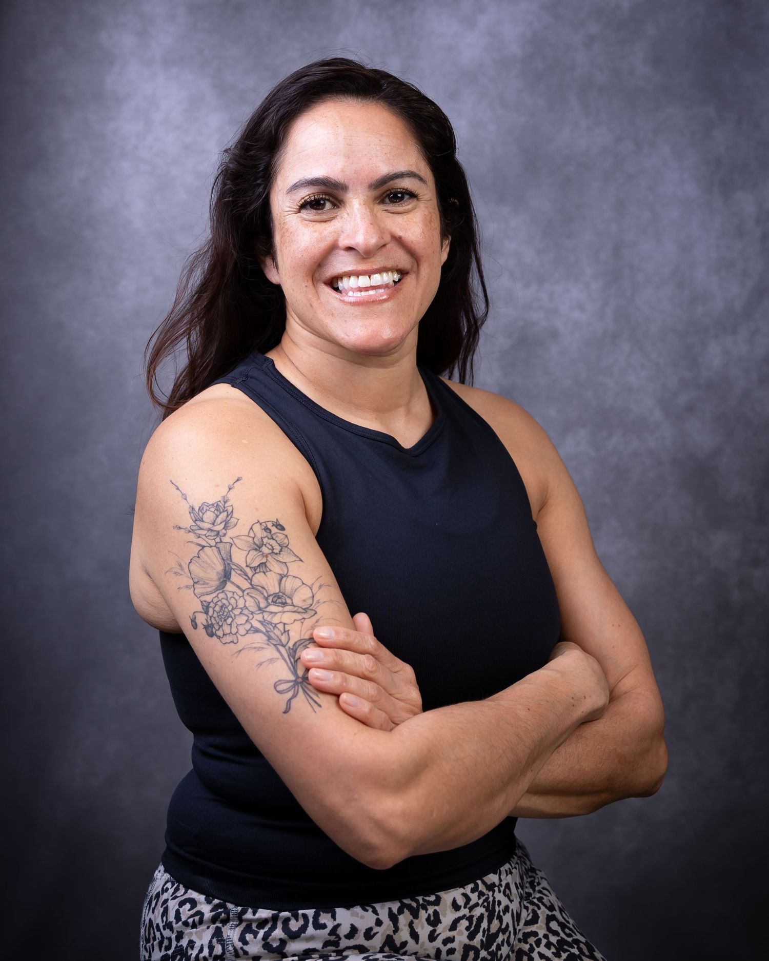 Professional portrait of someone in a black sleeveless top showing off a floral tattoo on their upper arm.
