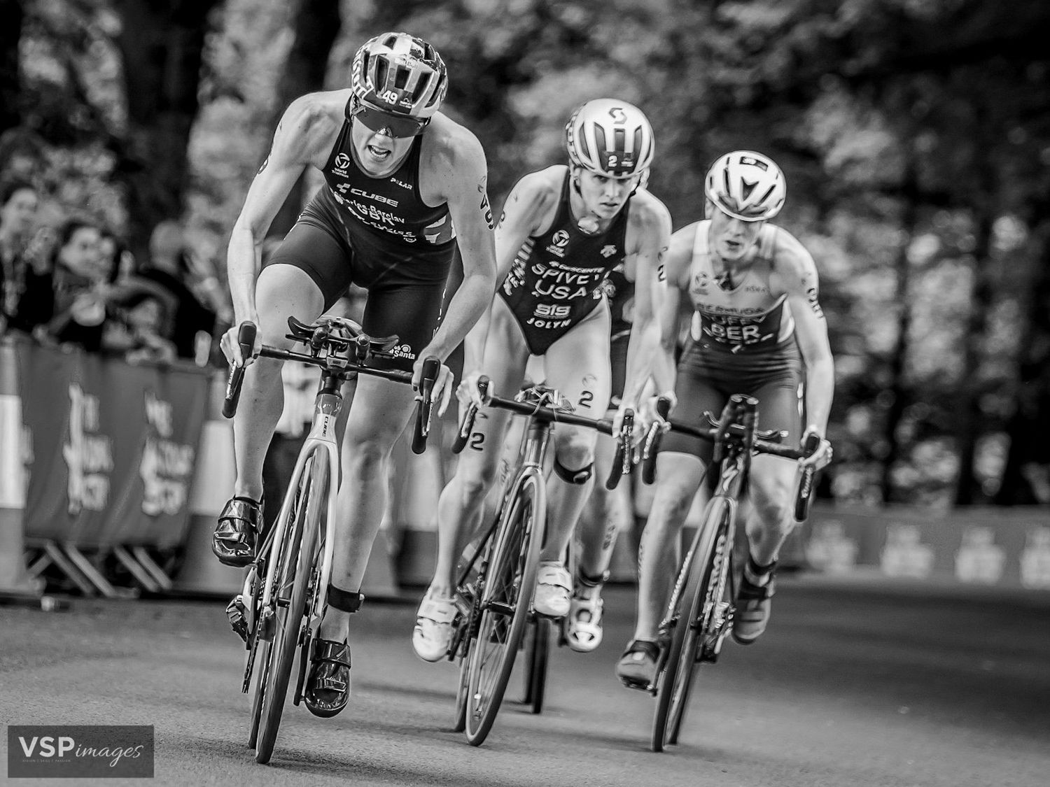 Professional triathletes racing in a cycling competition on road bikes in black and white monochrome photography.