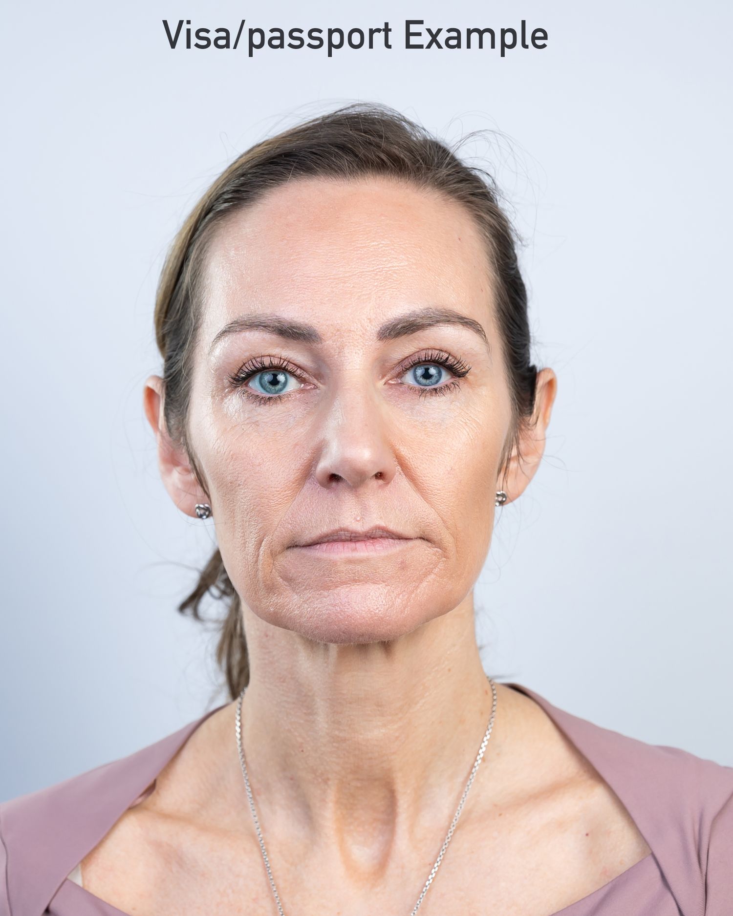 Professional passport photo of a person in a mauve top against a light gray background.