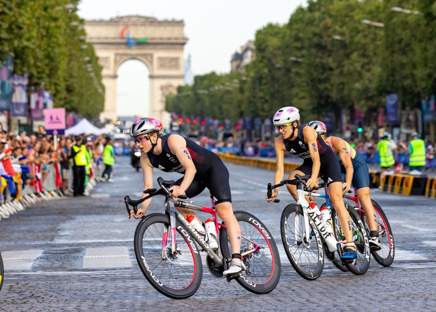 Cyclists race through the streets of Paris with the Arc de Triomphe visible in the background.