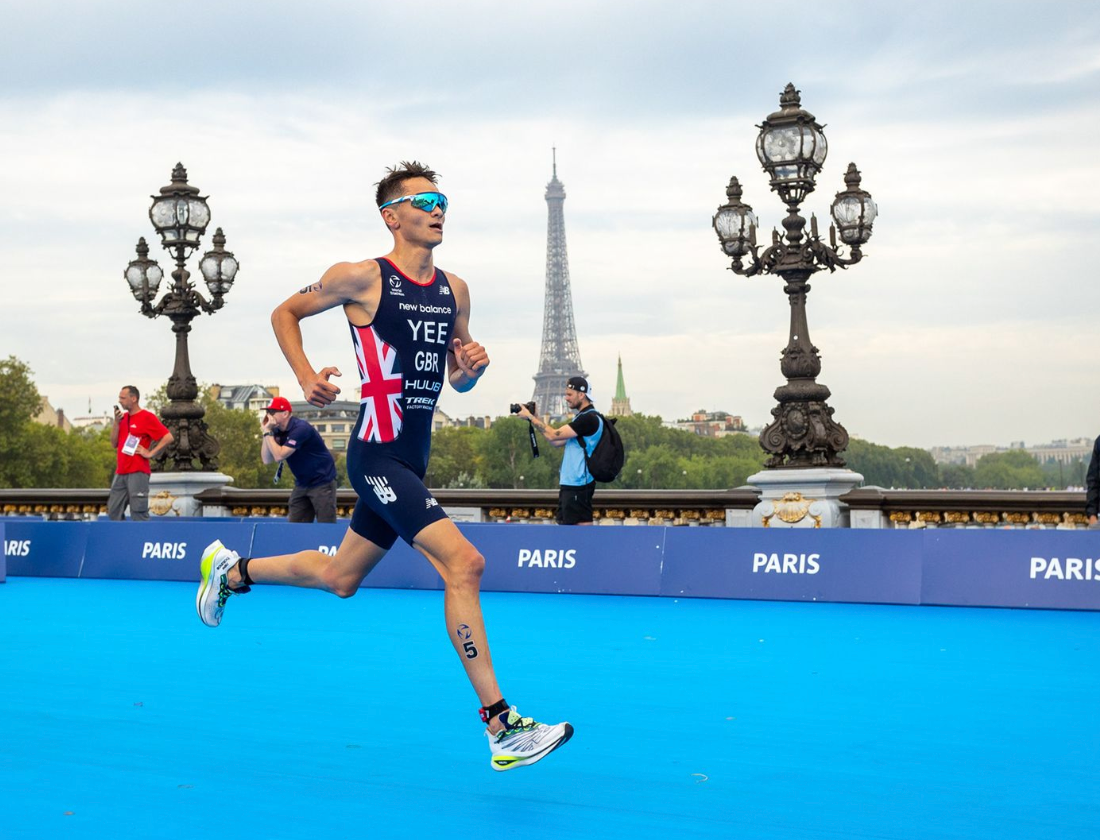 A triathlete races on a blue course in Paris with the Eiffel Tower visible in the background.