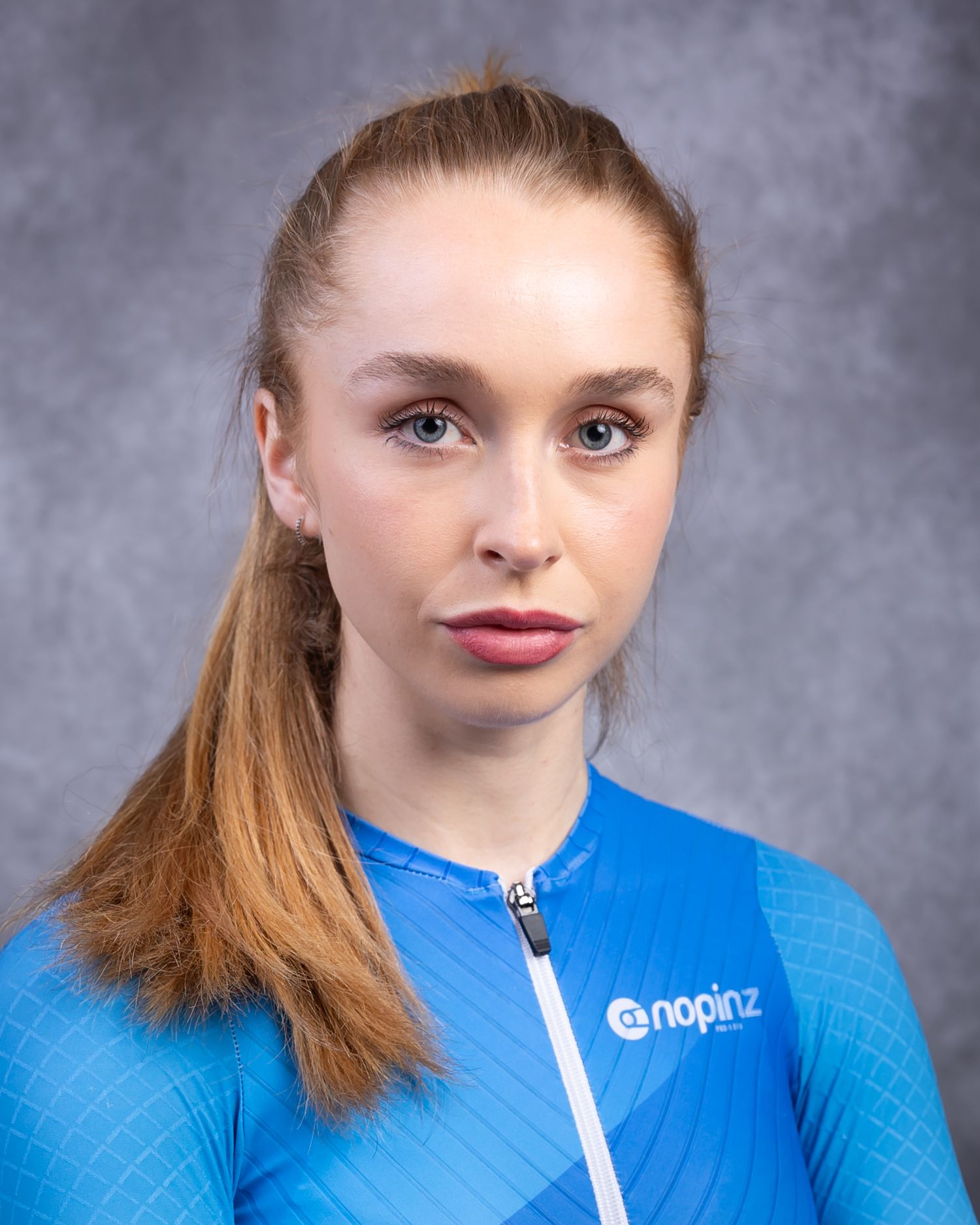 Portrait of someone with auburn hair wearing a bright blue shirt against a gray background.