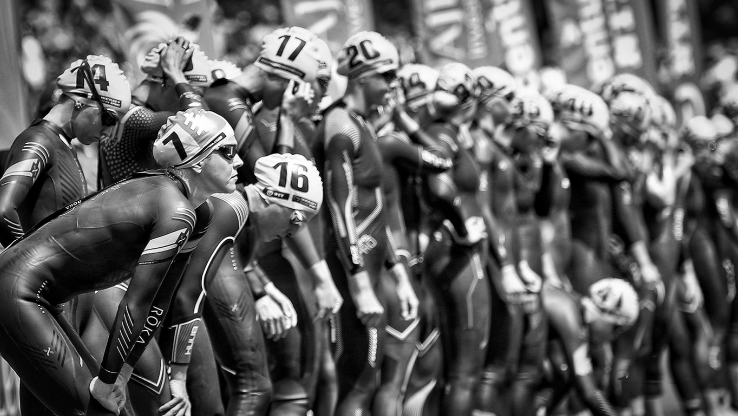 Black and white image of swimmers lined up at starting blocks before race.