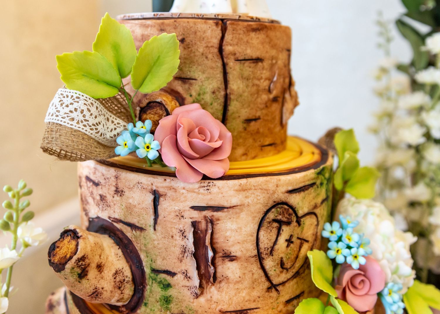 A rustic birch bark wedding cake decorated with pink roses and blue flowers.