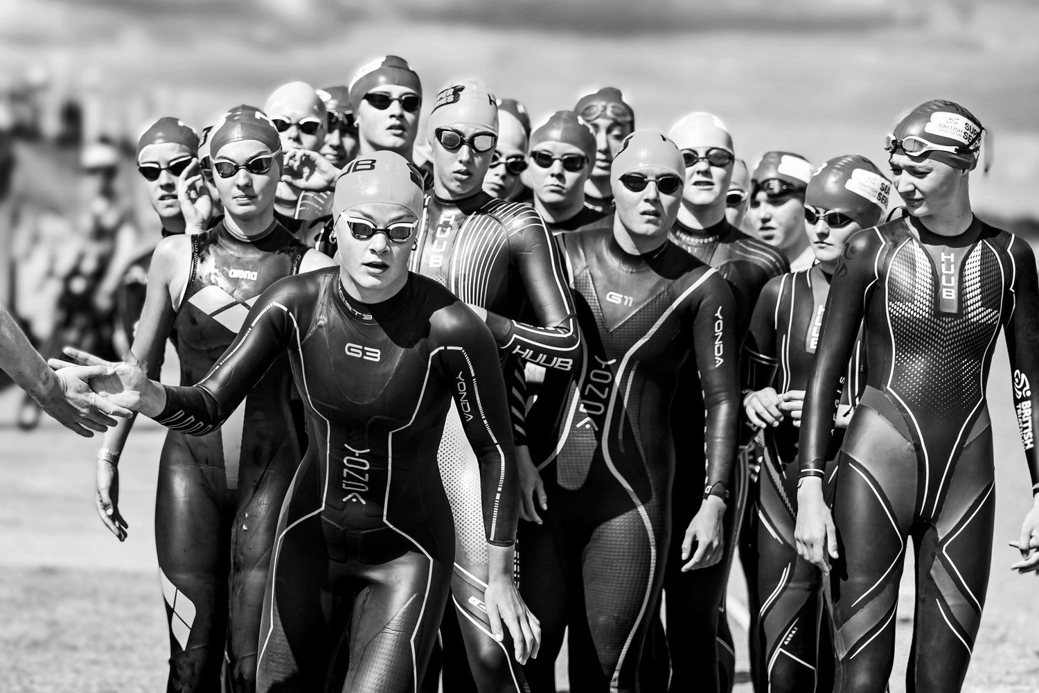 Black and white image of wetsuit-clad triathletes lined up before triathlon start.