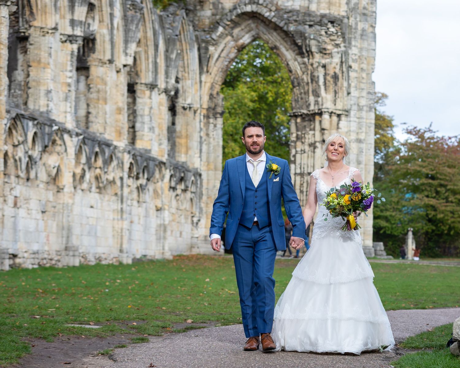 Wedding couple and bridal party walking along historic stone cathedral exterior.
