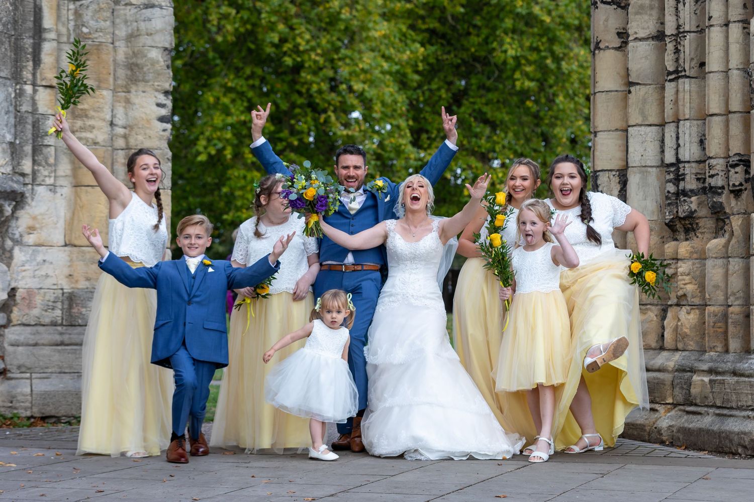 Wedding party poses in front of historic stone church with yellow and white attire.