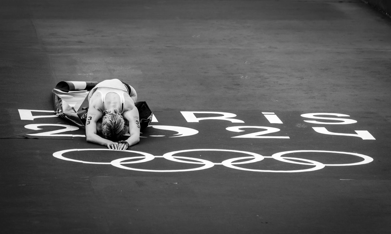A dramatic black and white photo of an athlete lying exhausted on a gym floor with painted markings.