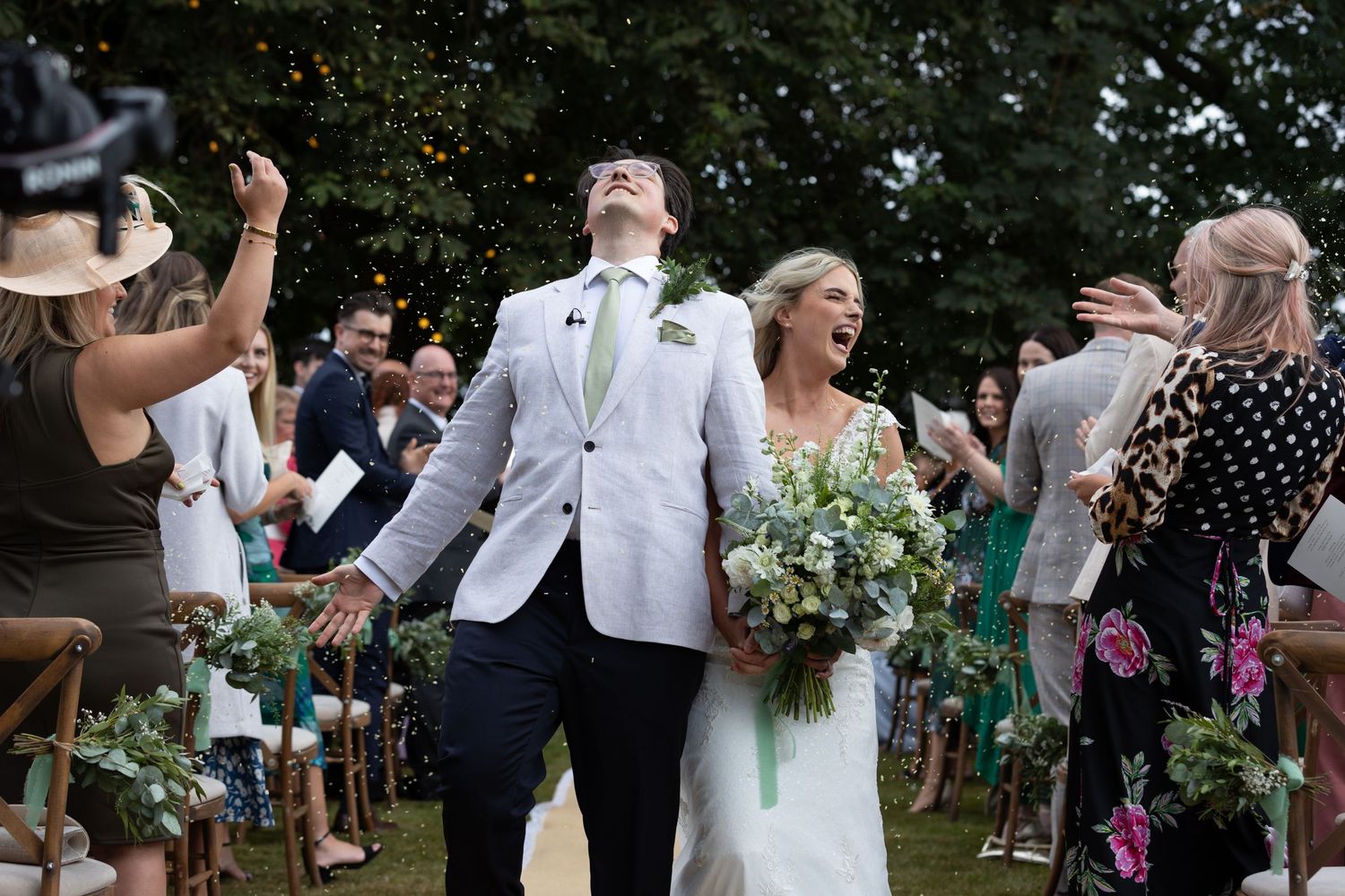 A couple celebrates while walking down the aisle at an outdoor wedding ceremony.