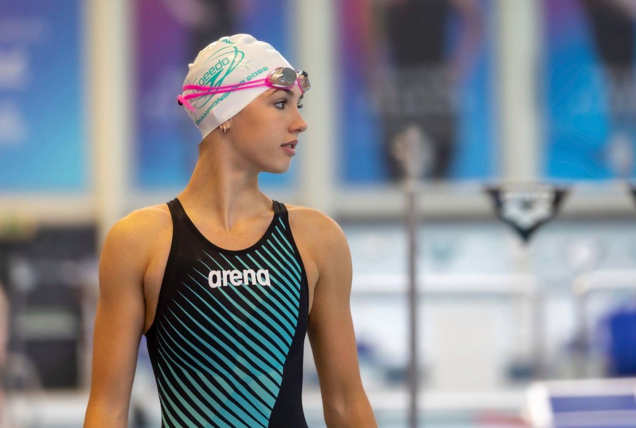 Competitive swimmer in black and teal Arena swimsuit and colorful swim cap at pool.