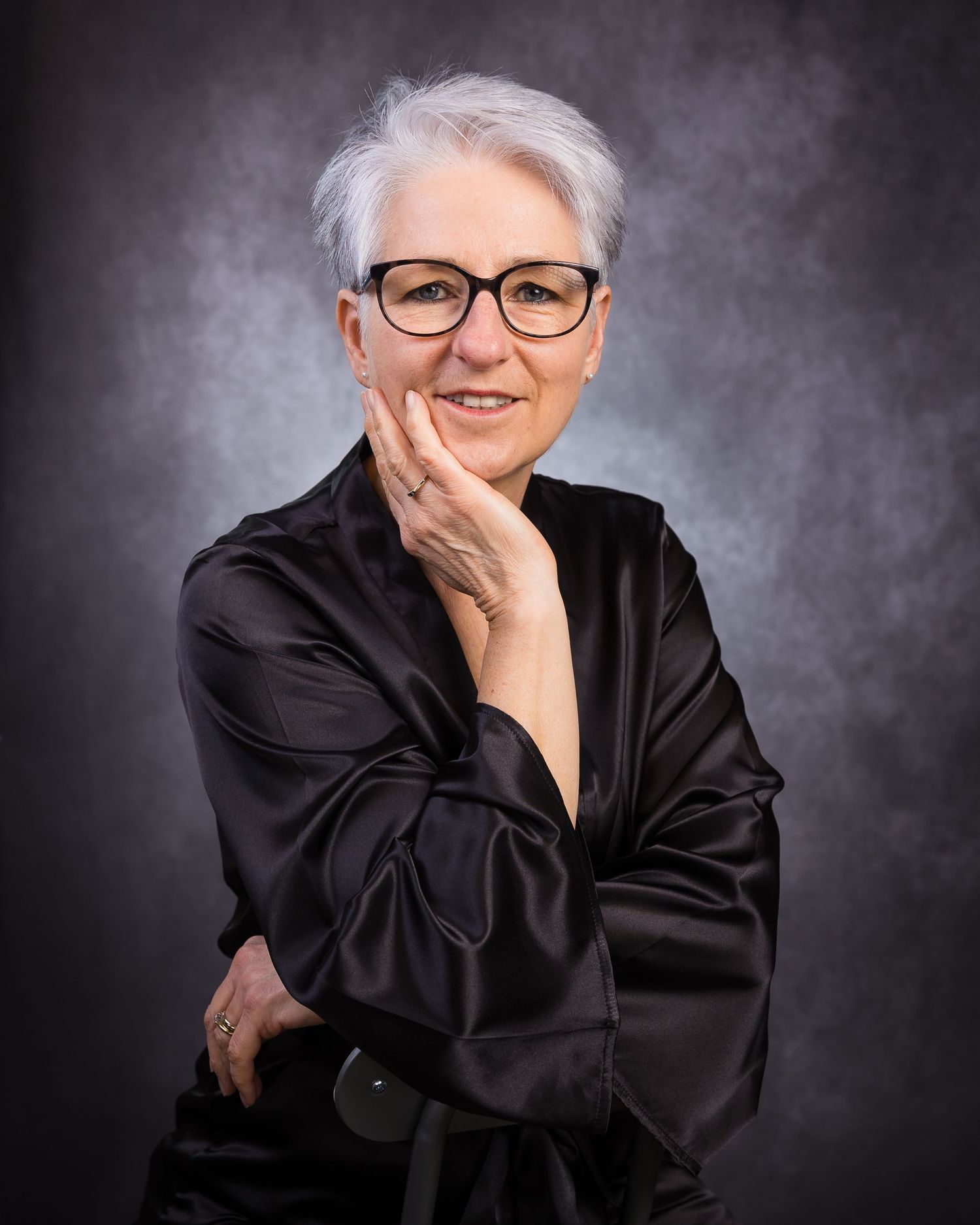 Professional studio portrait series showing person in black attire against dark gray backdrop with varying expressions.