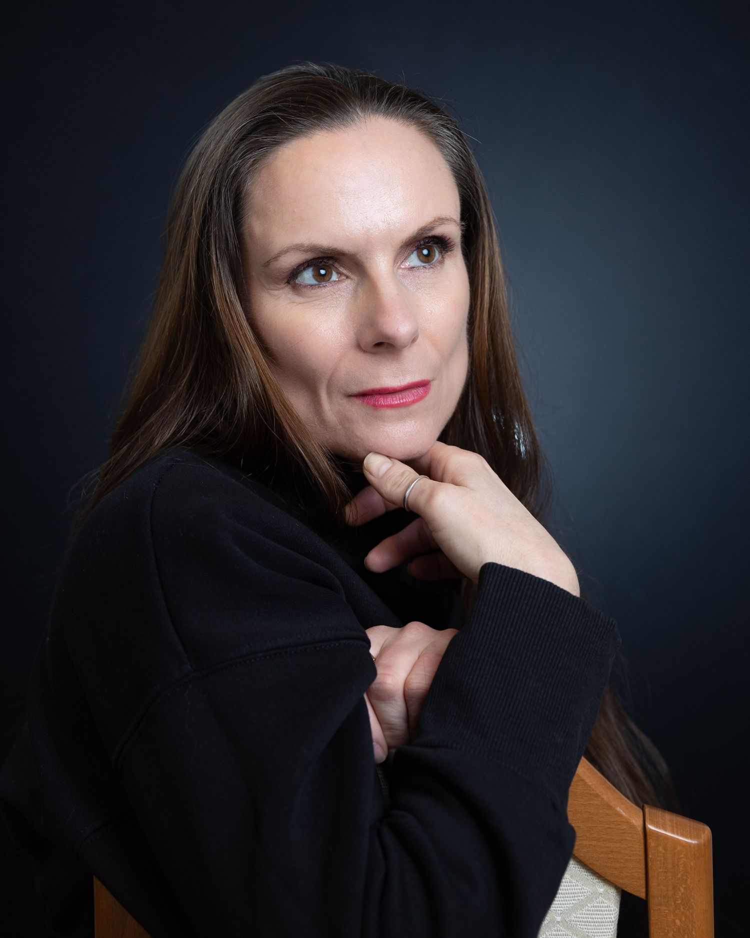 Professional studio portrait of a person in a black sweater with long dark hair against a dark background.