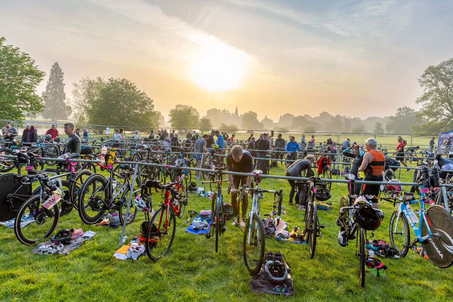 Rows of bicycles lined up at sunrise during a triathlon transition area on a misty morning.