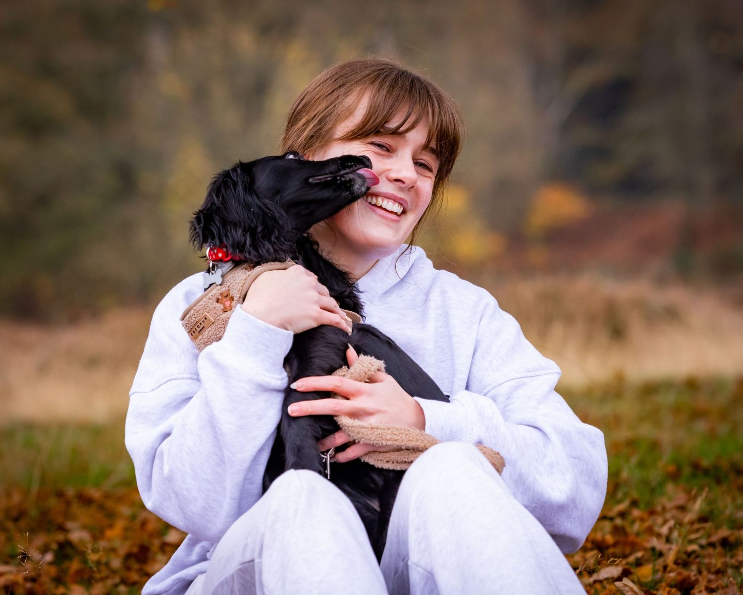 Small black dog receiving affectionate cuddles outdoors.