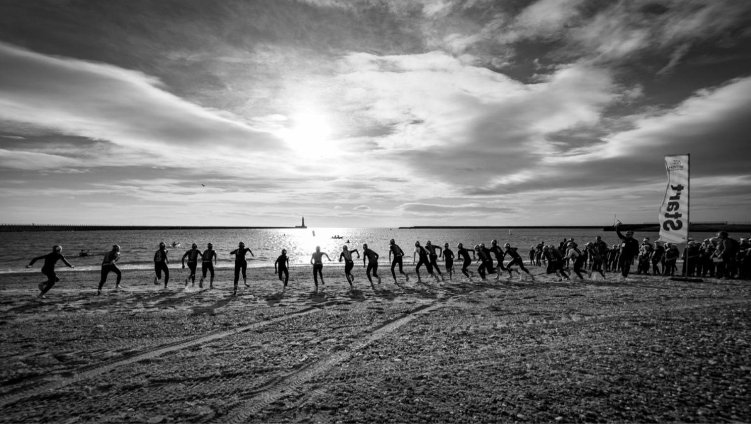 A silhouetted line of runners trains along a beach at sunset.