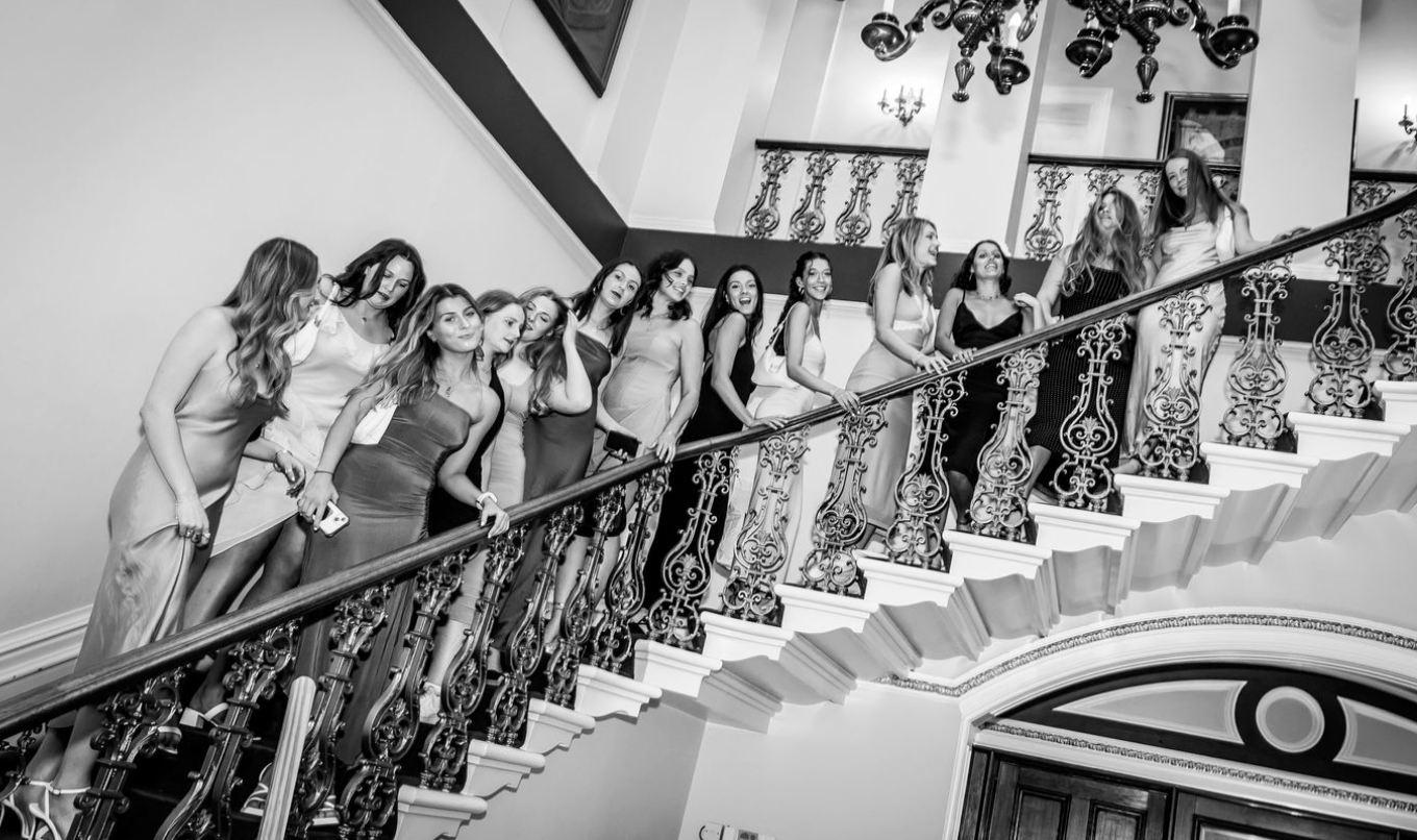Black and white photo of group posing on elegant curved staircase.