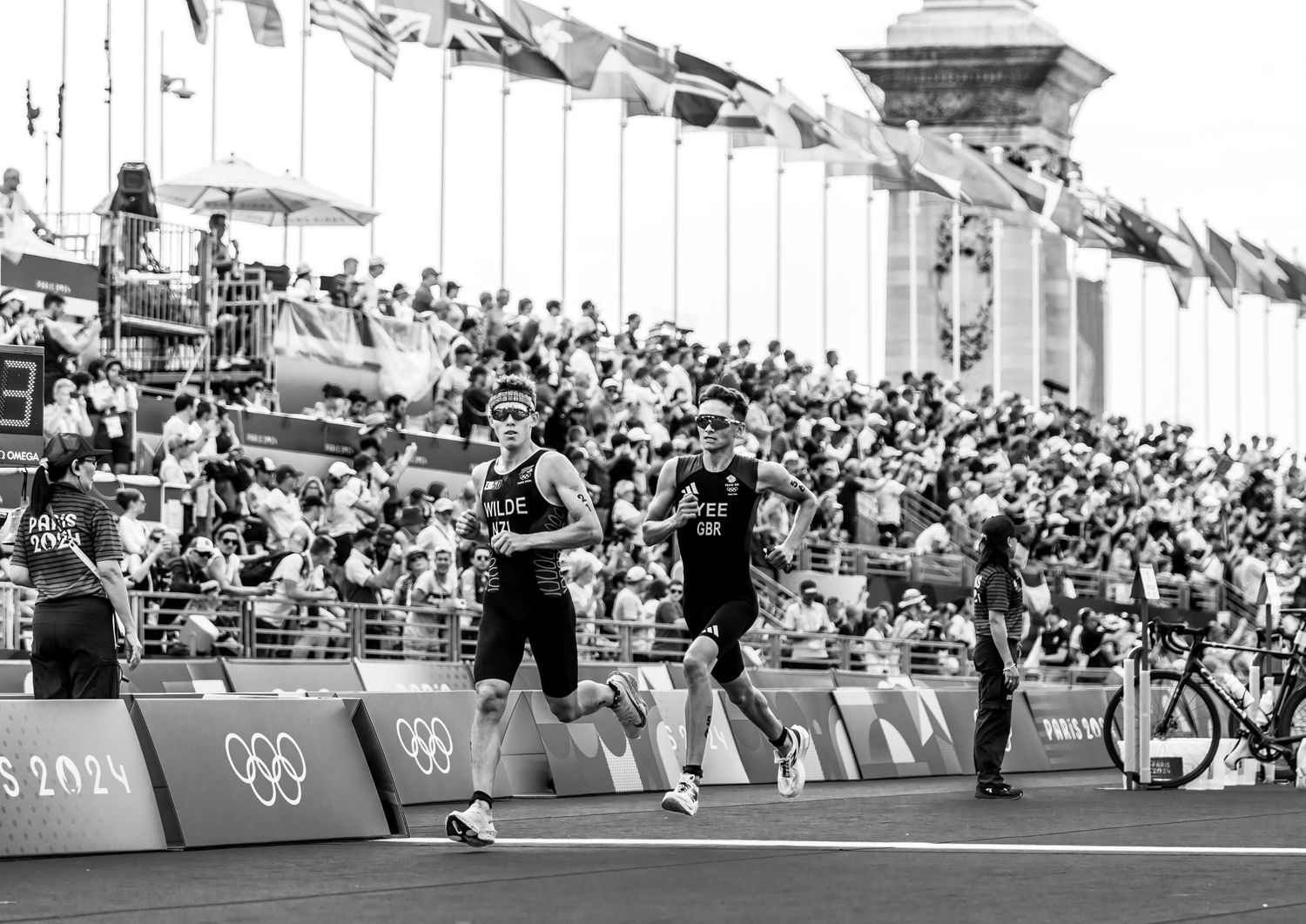 Olympic athletes racing on track with spectators watching from crowded stadium stands.