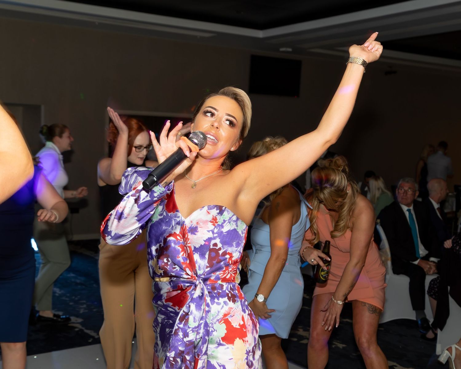 A performer in a floral dress sings enthusiastically at a wedding reception.