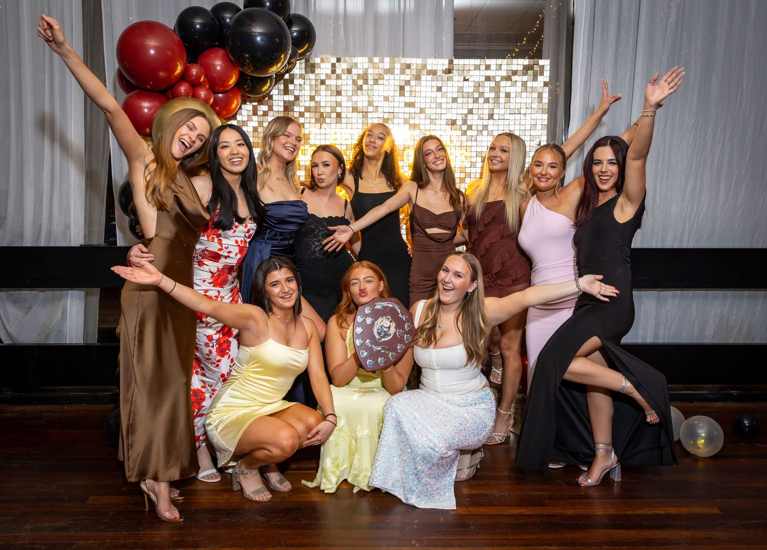 Group celebration photo with women in formal attire posing against a balloon backdrop.