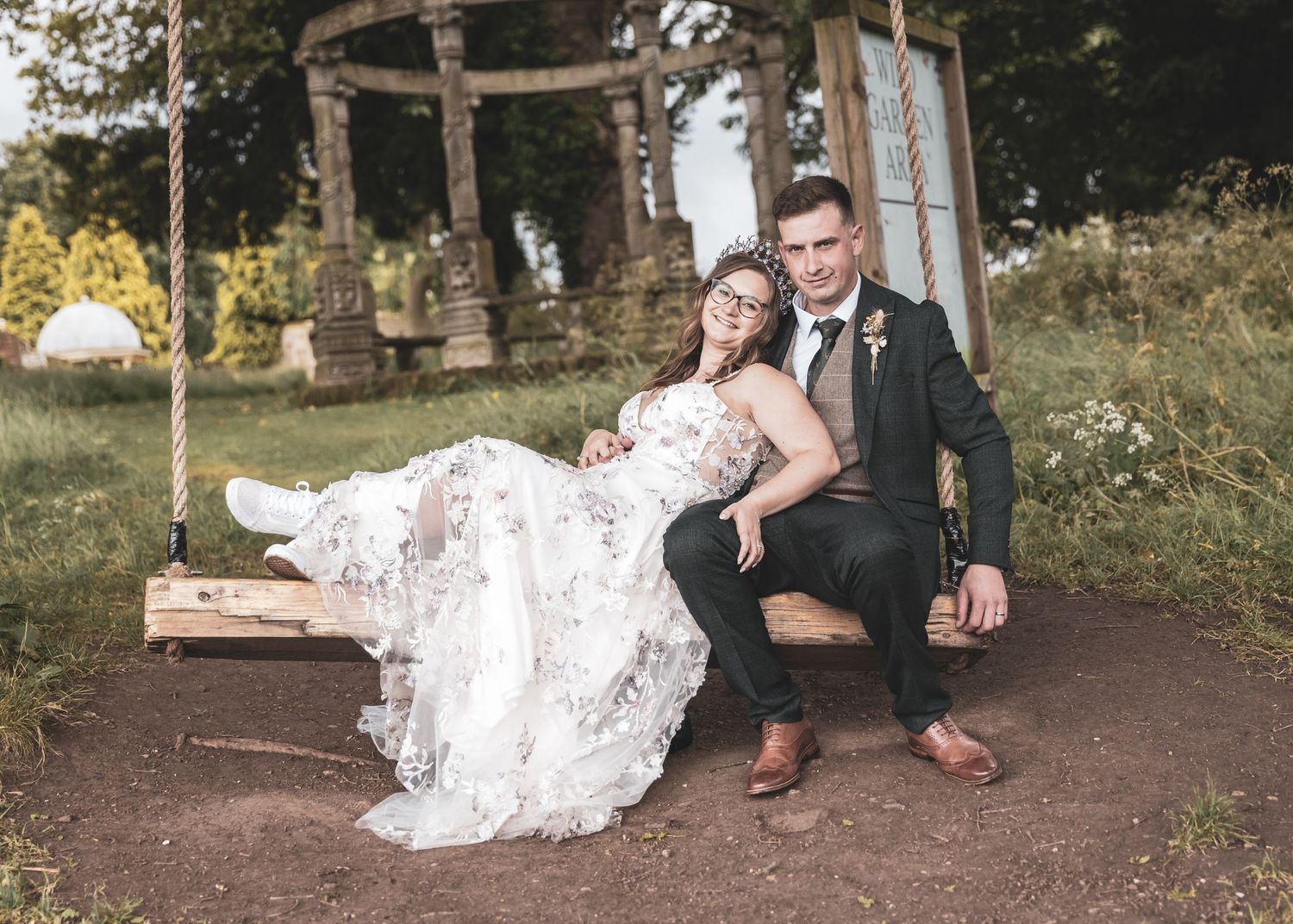 Wedding couple relaxes beneath trees in a rustic woodland setting.