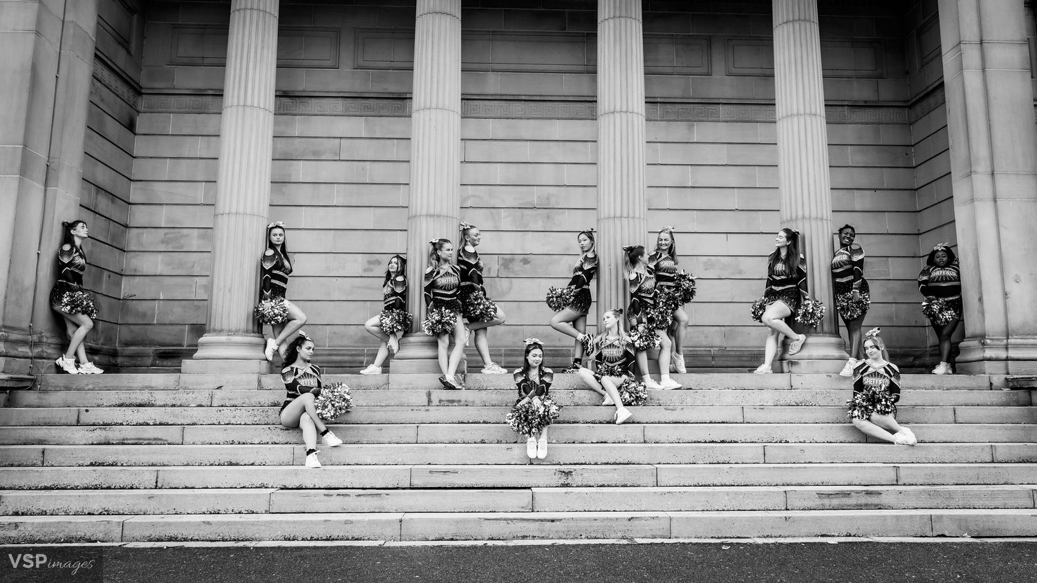 Black and white photo of cheerleading team arranged on historic building steps.