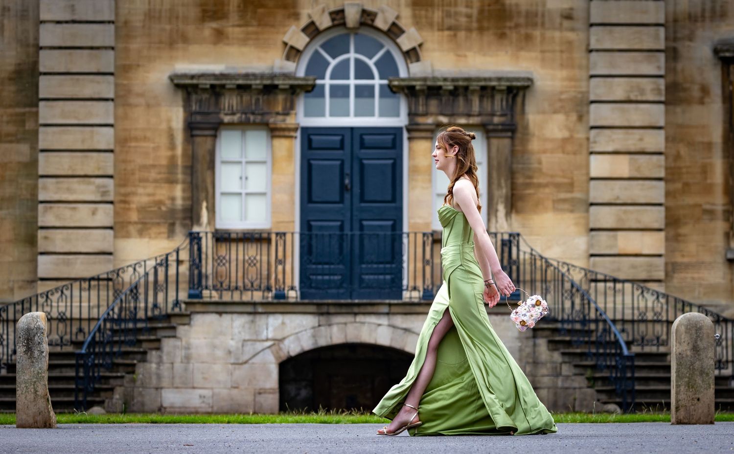 A person in an elegant green dress poses on historic stone steps of a classical building.