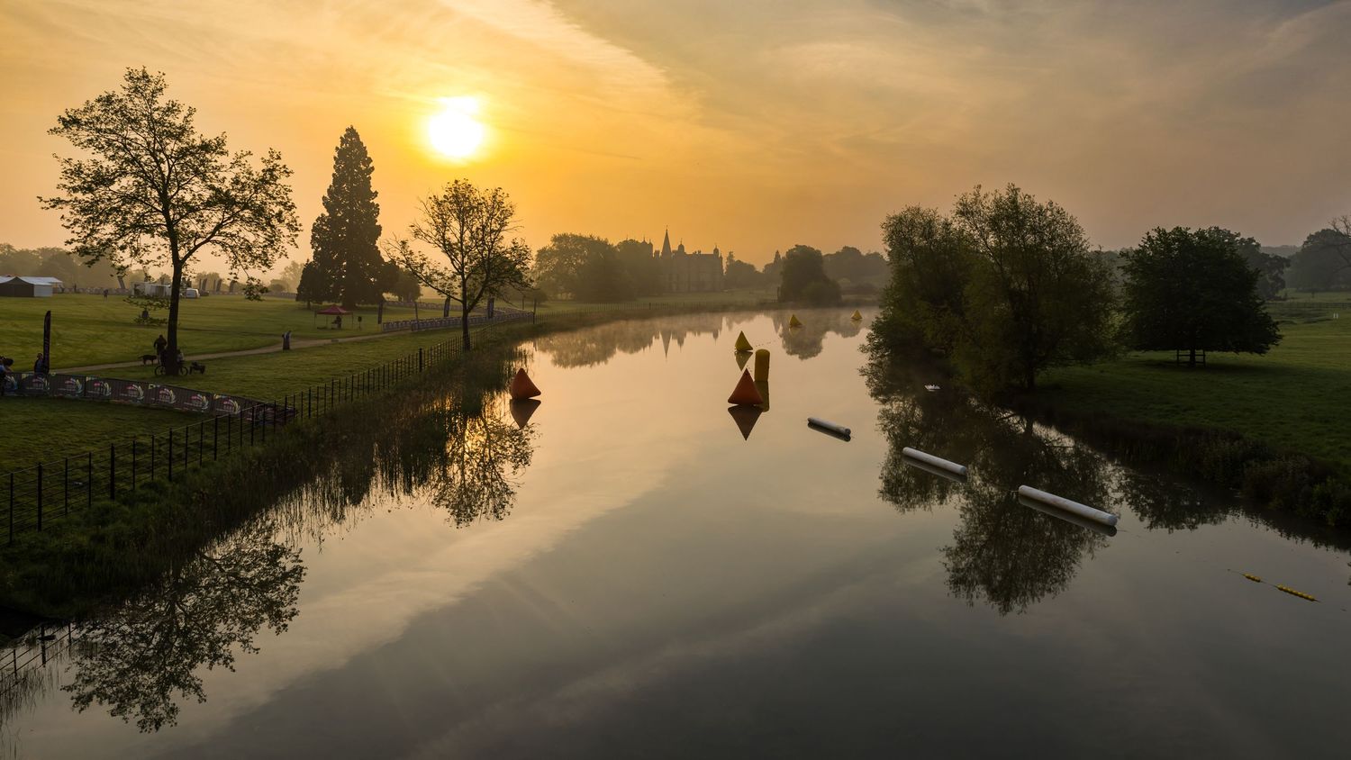 Tranquil sunset over a canal with trees silhouetted against an orange sky.