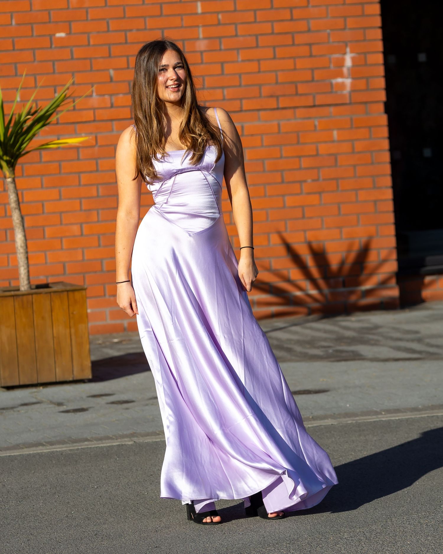A flowing lavender dress catches sunlight against rustic brick architecture.