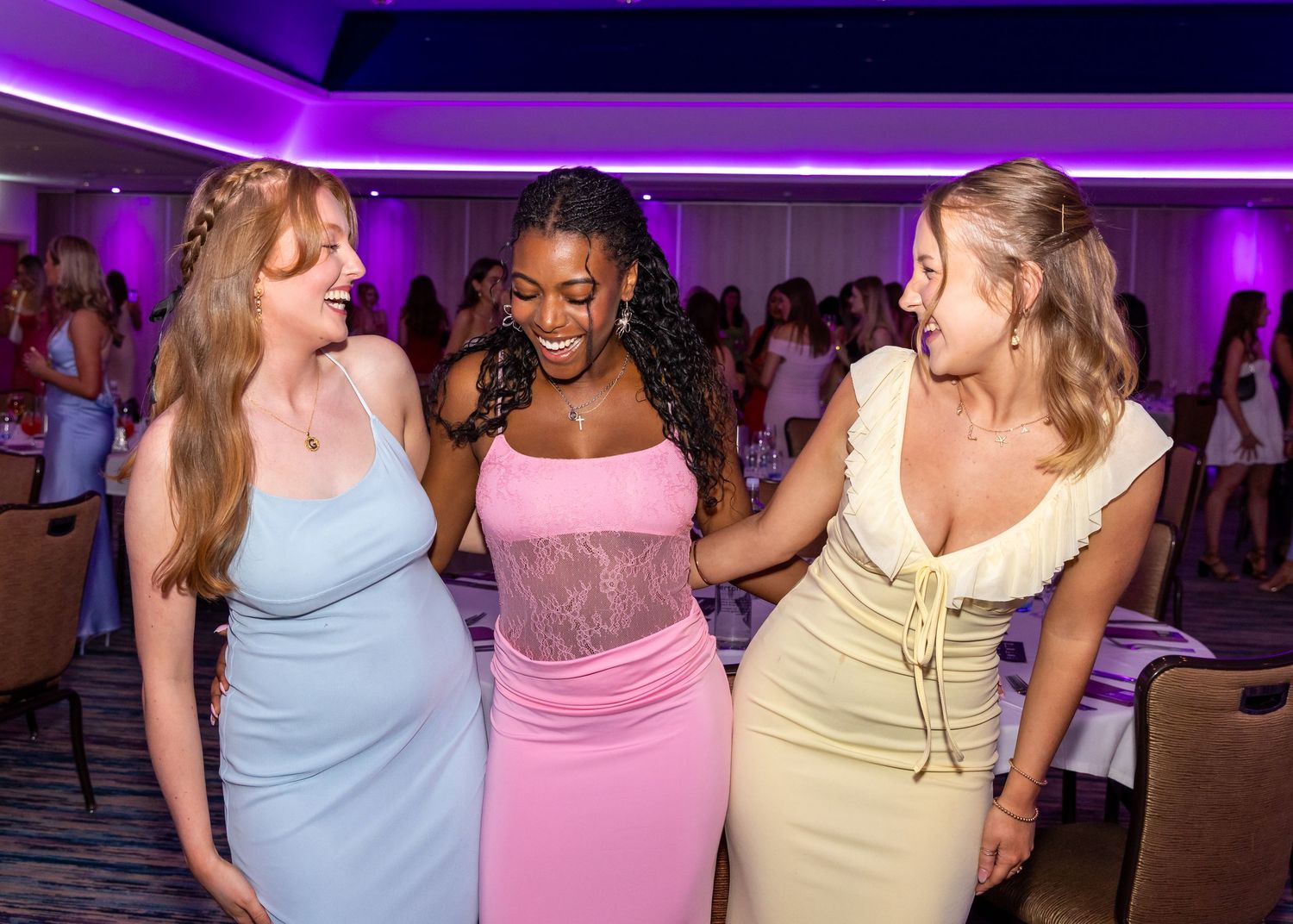 Three women in fitted dresses at a formal event with purple lighting.