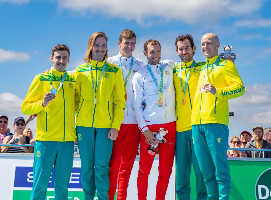 Athletes in yellow and green uniforms stand on a podium displaying their medals at an awards ceremony.