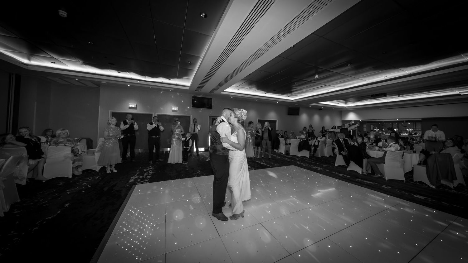 A couple shares their first dance on an illuminated white dance floor at their wedding reception.