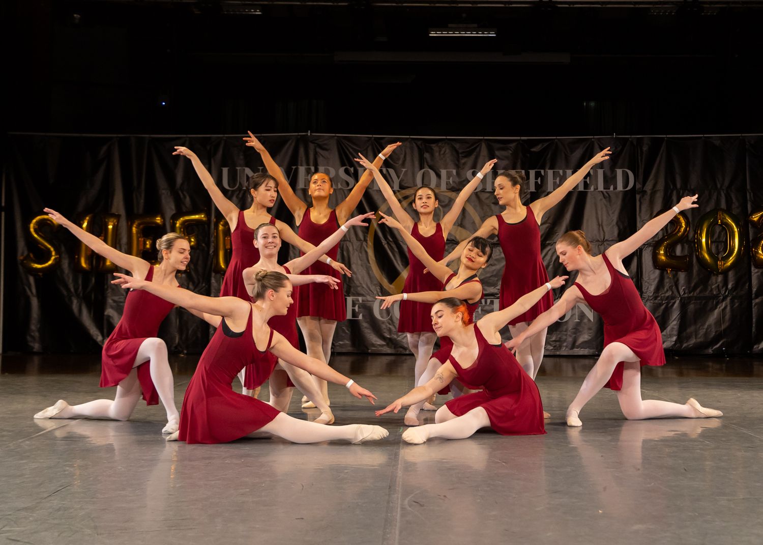 Dancers in flowing red dresses perform a synchronized routine on stage.
