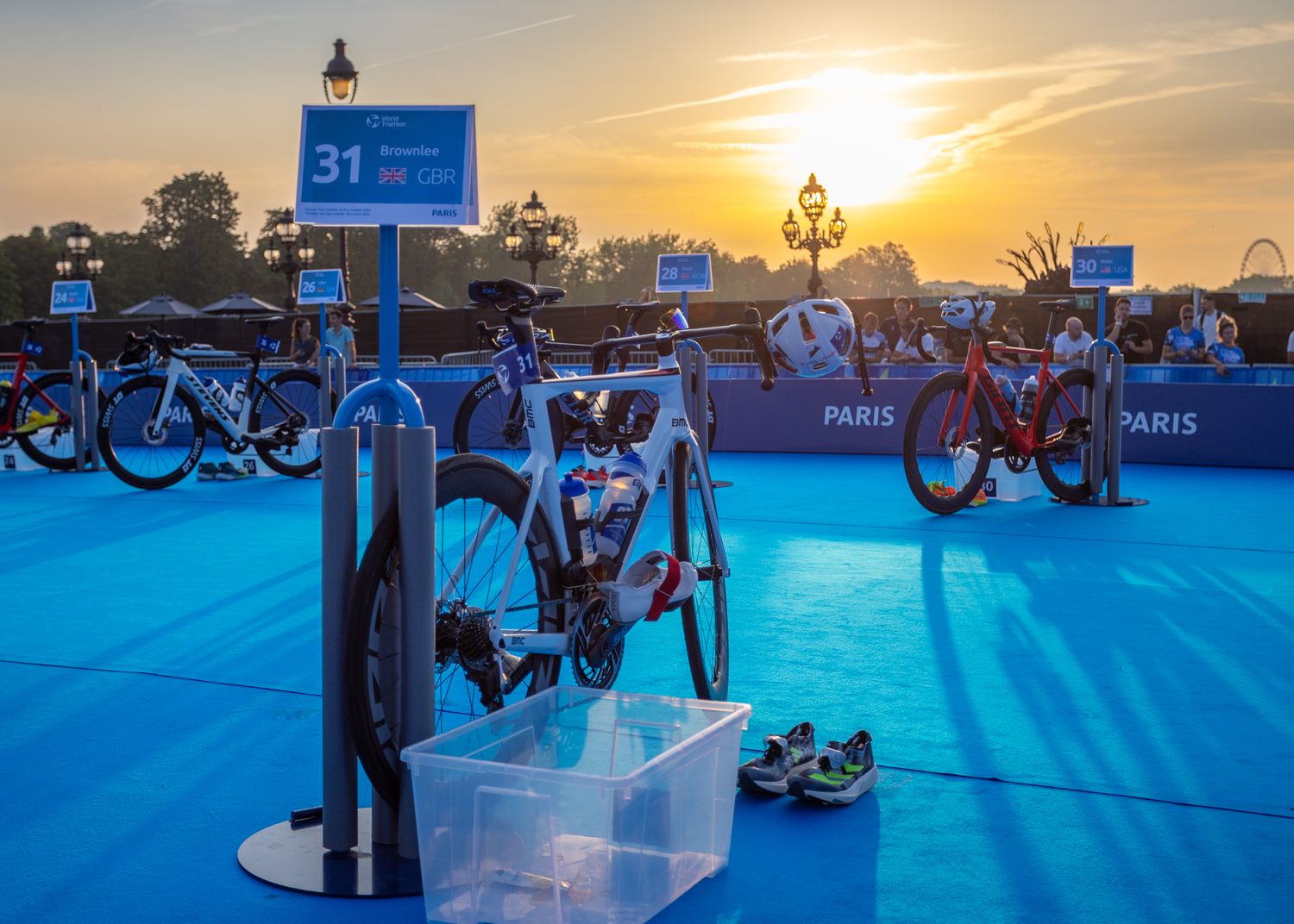 Triathlon transition area at sunset with bikes lined up against blue backdrop.
