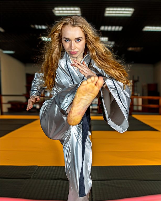 A martial artist performs a dynamic kick wearing a metallic uniform in a training facility.